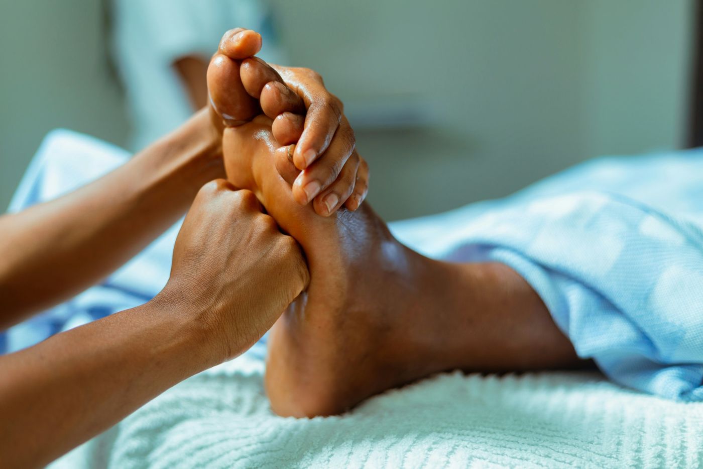 Hands gently holding and working on a client's foot as they rest under a soft blanket